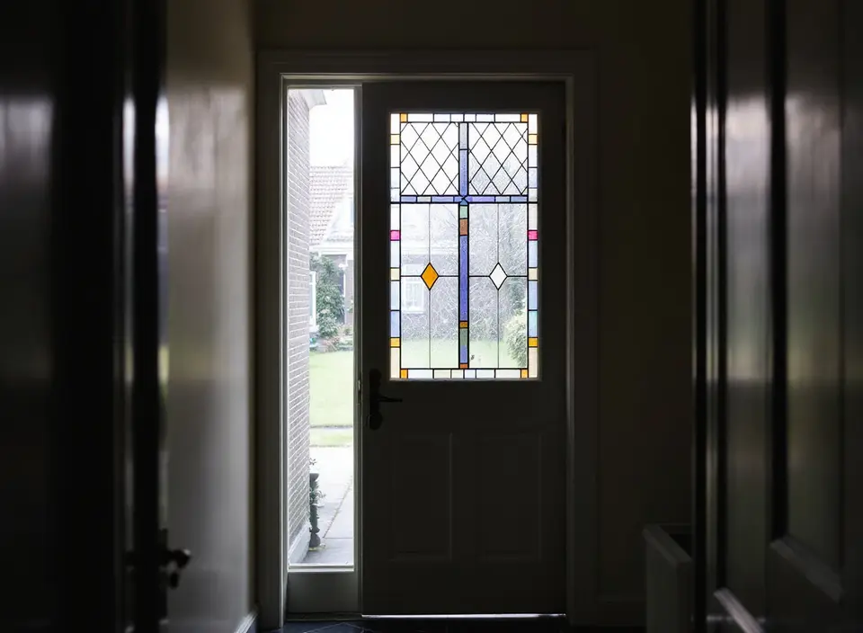 Een gang in een oud huis met een glas-in-loodraam in de voordeur, van binnen gezien, met daglicht en een tuin erachter